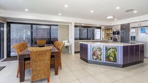 A modern kitchen with a central island, dining area with wicker chairs, and a view through large windows.