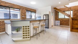 A modern kitchen with a brick accent wall, a bar area with stools, and a staircase leading to an upper level.