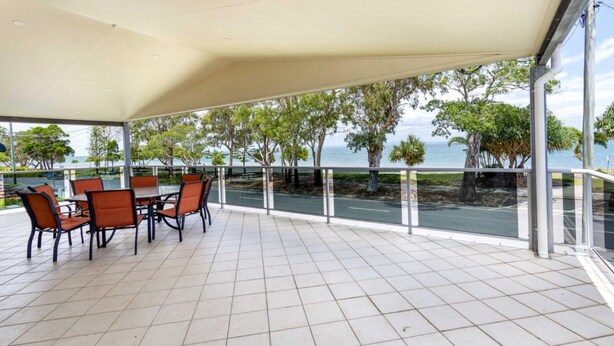 A covered outdoor seating area with a view of the sea and trees.