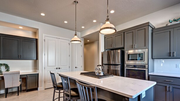 Une cuisine moderne avec des meubles de couleur sombre, un îlot en marbre, des appareils électroménagers en acier inoxydable et des luminaires suspendus.