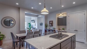 Une cuisine moderne dotée d’un îlot central, de meubles de rangement aux couleurs sombres et d’un éclairage suspendu.