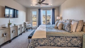 Une chambre à coucher comprenant un lit, une télévision, un ventilateur de plafond, un bureau et une vue sur l’extérieur.