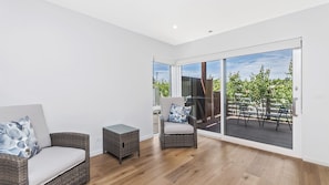 A modern living room with a sofa, a chair, a small table, and a large sliding glass door leading to an outdoor deck. - Cosmopolitan living located in a premium spot on the Moyne River (PORT FAIRY)