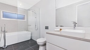 Une salle de bain moderne équipée d’une baignoire, d’une douche, de toilettes et d’un grand miroir.