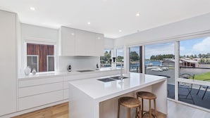 Une cuisine moderne avec des meubles blancs, un grand îlot central doté de tabourets et une vue sur une marina, visible à travers de grandes fenêtres.