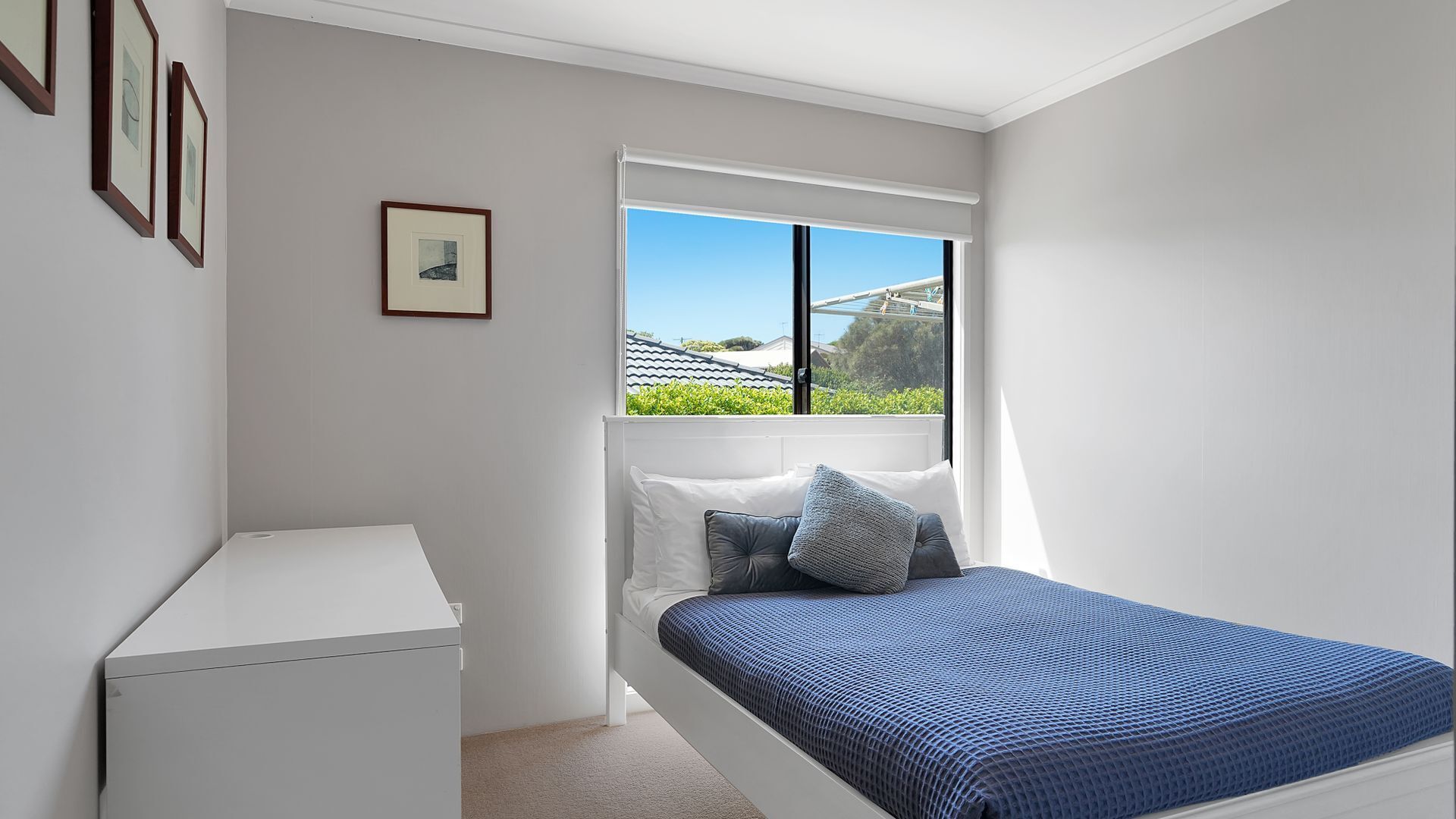 A bedroom with a bed, a window, and a small white cabinet.
