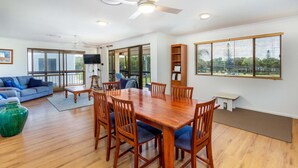 A spacious living room with a wooden dining table, blue sofas, and a large window with blinds. - Spacious Unit Overlooking Moreton Bay (WOORIM)