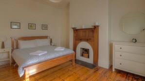 A bedroom with a wooden bed, a fireplace, a dresser, and a mirror. - Traditional historic cottage in a central location. (Port Fairy)