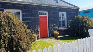 A house with a red door, two windows, and a white picket fence. - Traditional historic cottage in a central location. (Port Fairy)