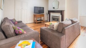 A living room with two sofas, a coffee table, a TV, and a fireplace. - Traditional historic cottage in a central location. (Port Fairy)