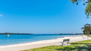 Una spiaggia con una panchina, acqua cristallina e una barca a vela all'orizzonte.