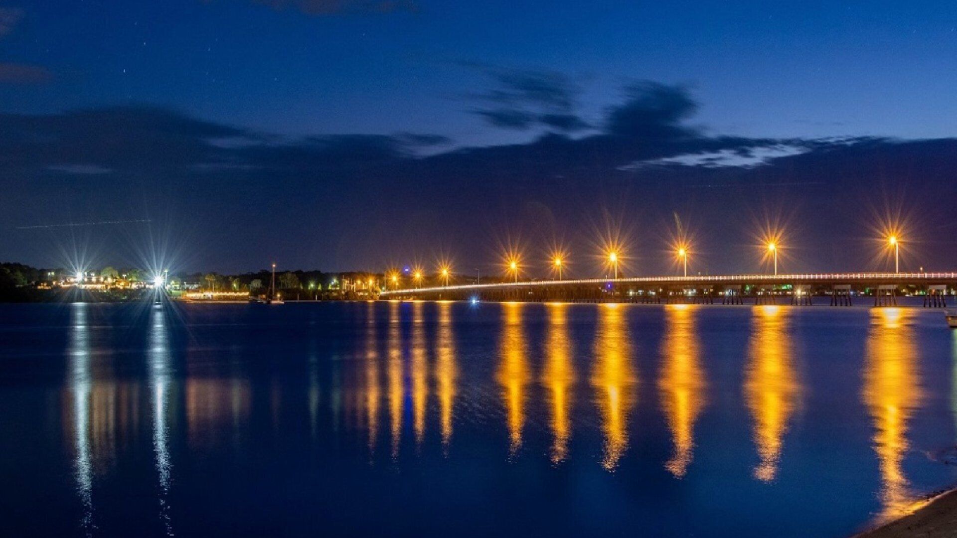 A nighttime view of a bridge with lights reflecting on the water.