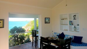 Une chambre dotée d’un balcon donnant sur la côte, d’un ventilateur de plafond et d’un coin repas avec une table et des chaises.