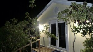 Un petit bâtiment blanc doté d’une terrasse en bois et d’une porte à panneaux de verre.