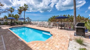 A pool area with lounge chairs and umbrellas, a grill, and a view of the ocean. - Family-Friendly 3BR Beachfront Retreat | Indian Rocks | Sea Side #202 (Indian Rocks Beach)