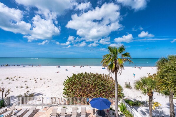 A beach with white sand, palm trees, and a clear blue sky.