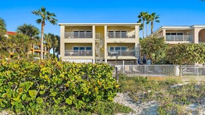 A two-story hotel with balconies, a sandy beach in front, and palm trees. - Family-Friendly 3BR Beachfront Retreat | Indian Rocks | Sea Side #202 (Indian Rocks Beach)