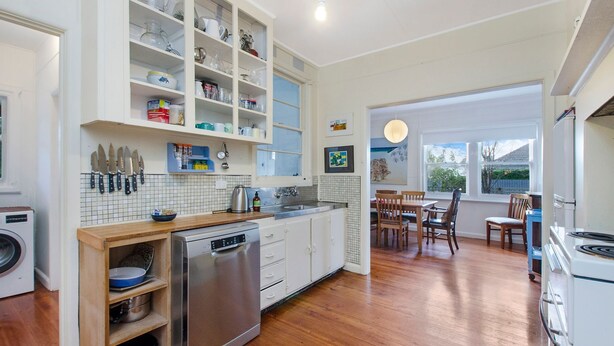 A modern kitchen with white cabinets, a stainless steel refrigerator, and a wooden dining table with chairs. - A quaint artistic cottage for all seasons (PORT FAIRY)