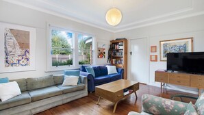 A living room with a grey sofa, a blue sofa, a wooden coffee table, a TV on a wooden stand, and a bookshelf. - A quaint artistic cottage for all seasons (PORT FAIRY)