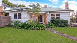 A two-story house with a front porch, brick chimney, and a well-maintained lawn. - A quaint artistic cottage for all seasons (PORT FAIRY)