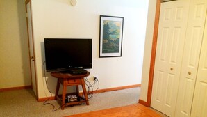 Una habitación con una mesa de madera, un televisor sobre un mueble, un cuadro en la pared y una puerta.