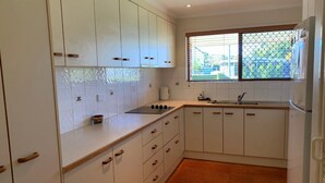 A kitchen with white cabinets, a black countertop, a window with blinds, and a refrigerator. - Lowset Pet Friendly Home (BONGAREE)