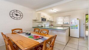 A compact kitchen with white cabinets, a microwave, a refrigerator, and a clock on the wall. - Bribie Waters On Welsby (BONGAREE)