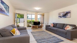 A living room with a grey sofa, a grey armchair, a TV on a wooden stand, and a patterned rug. - Bribie Waters On Welsby (BONGAREE)