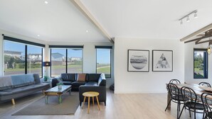 A spacious living area with a sofa, coffee table, and dining table. Large windows offer views of the outside.