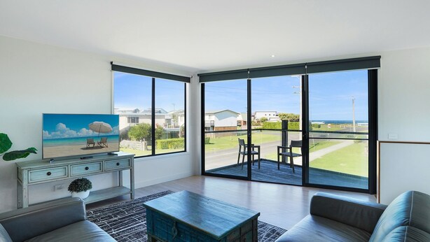 A spacious living room with large windows, a flat-screen TV, a coffee table, and a sofa.