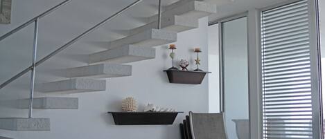 A modern interior with a concrete staircase, wall-mounted shelves with decorative items, and a seating area with chairs.