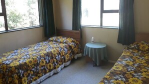 Una stanza con due letti singoli, un tavolino rotondo e ampie finestre con tende.
