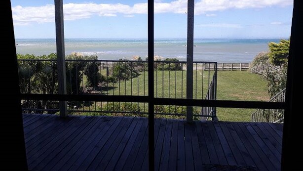 Un pontile in legno con vista sull'oceano e una zona erbosa delimitata da una recinzione.