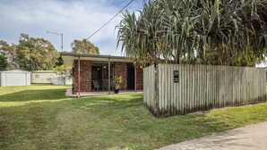 A single-story building with a patio, a fenced area with a sign '29 Wattle Avenue,' and a grassy yard. - Bongaree Retreat With Room For The Boat (BONGAREE)