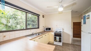 A kitchen with a microwave, stove, sink, and a window with a view of greenery. - Bongaree Retreat With Room For The Boat (BONGAREE)