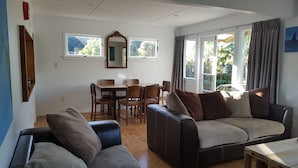 A living room with a sofa, a dining table with chairs, and a large window with curtains.