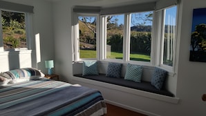 A bedroom with a large window seat, a bed with striped bedding, and a nightstand with a lamp.