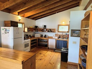 A compact kitchen with wooden beams, a refrigerator, stove, microwave, sink, and various kitchen items.