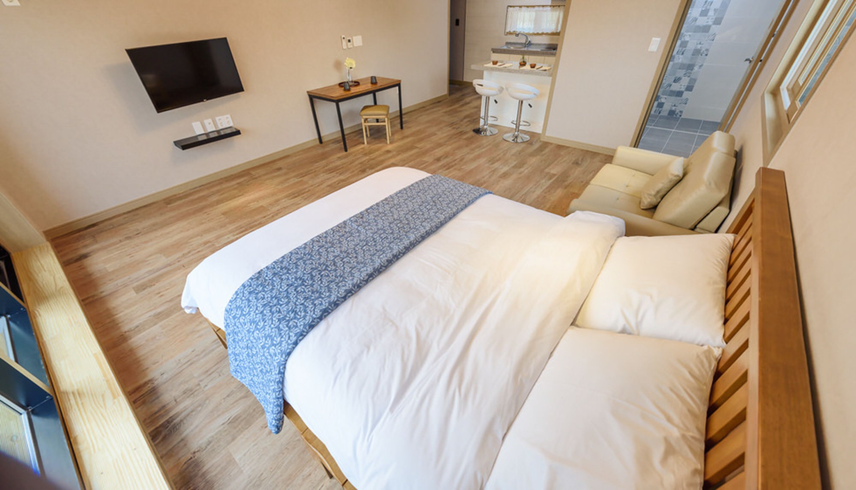 Hotellihuone, jossa on suuri sänky, seinälle asennettu televisio, pieni pöytä ja tuoli, kylpyhuone, jossa on pesuallas ja peili, sekä ikkuna, josta on näkymä ulos.