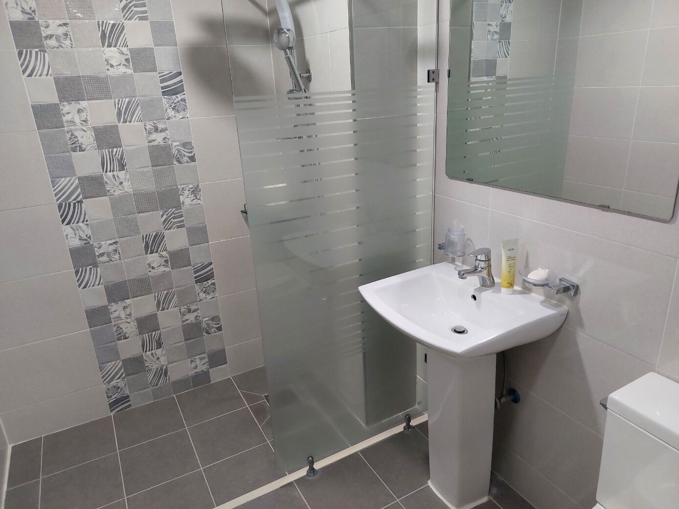 A bathroom with a white sink, a glass shower enclosure, and patterned tiles on the walls.