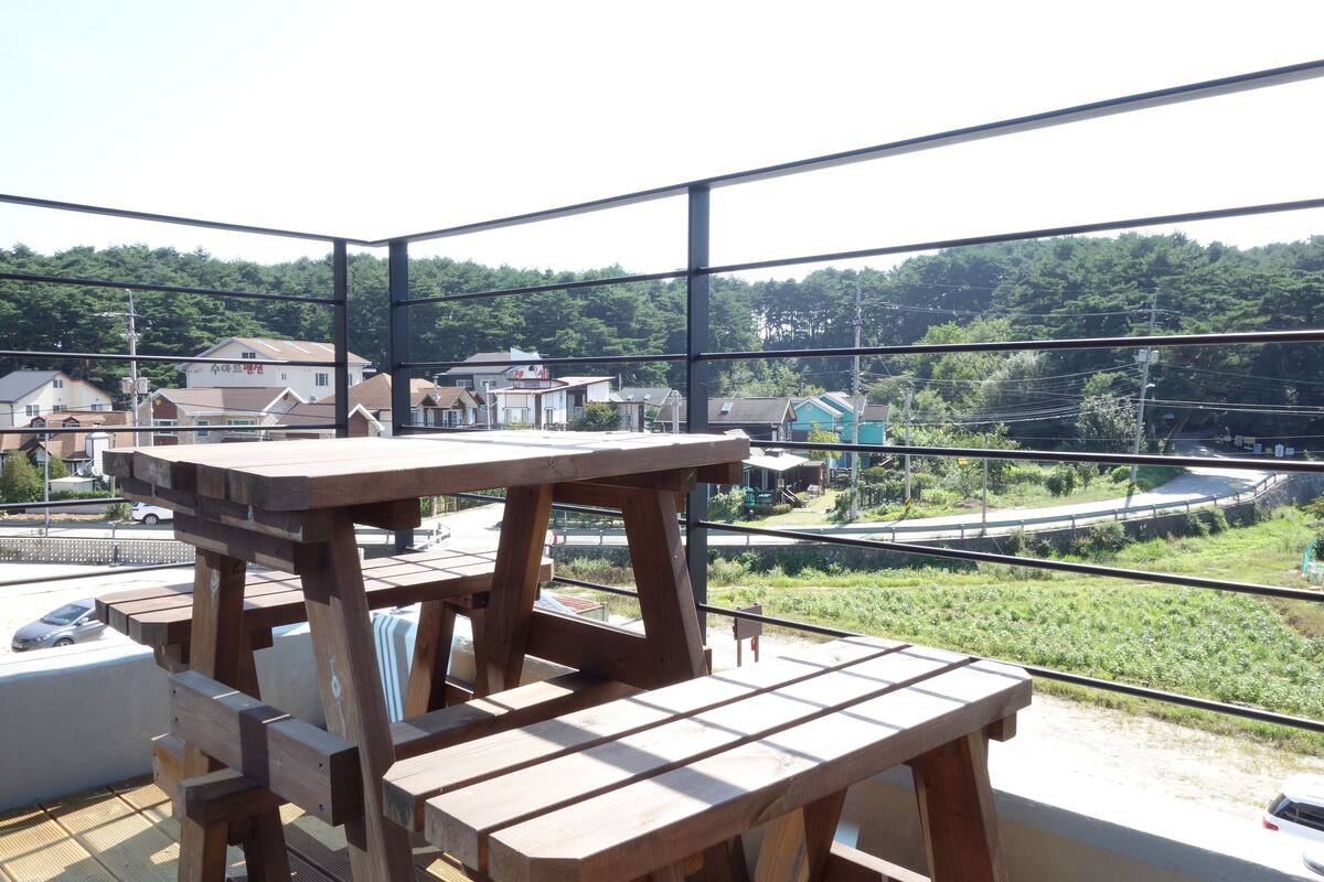 Ein Holztisch und eine Bank auf einem Balkon mit Blick auf Häuser und Grünflächen.