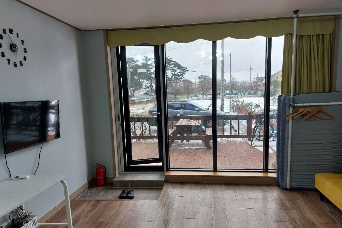 Ein Zimmer mit einer großen Schiebetür zu einem Außenbereich mit Holzterrasse und Blick auf eine verschneite Landschaft.