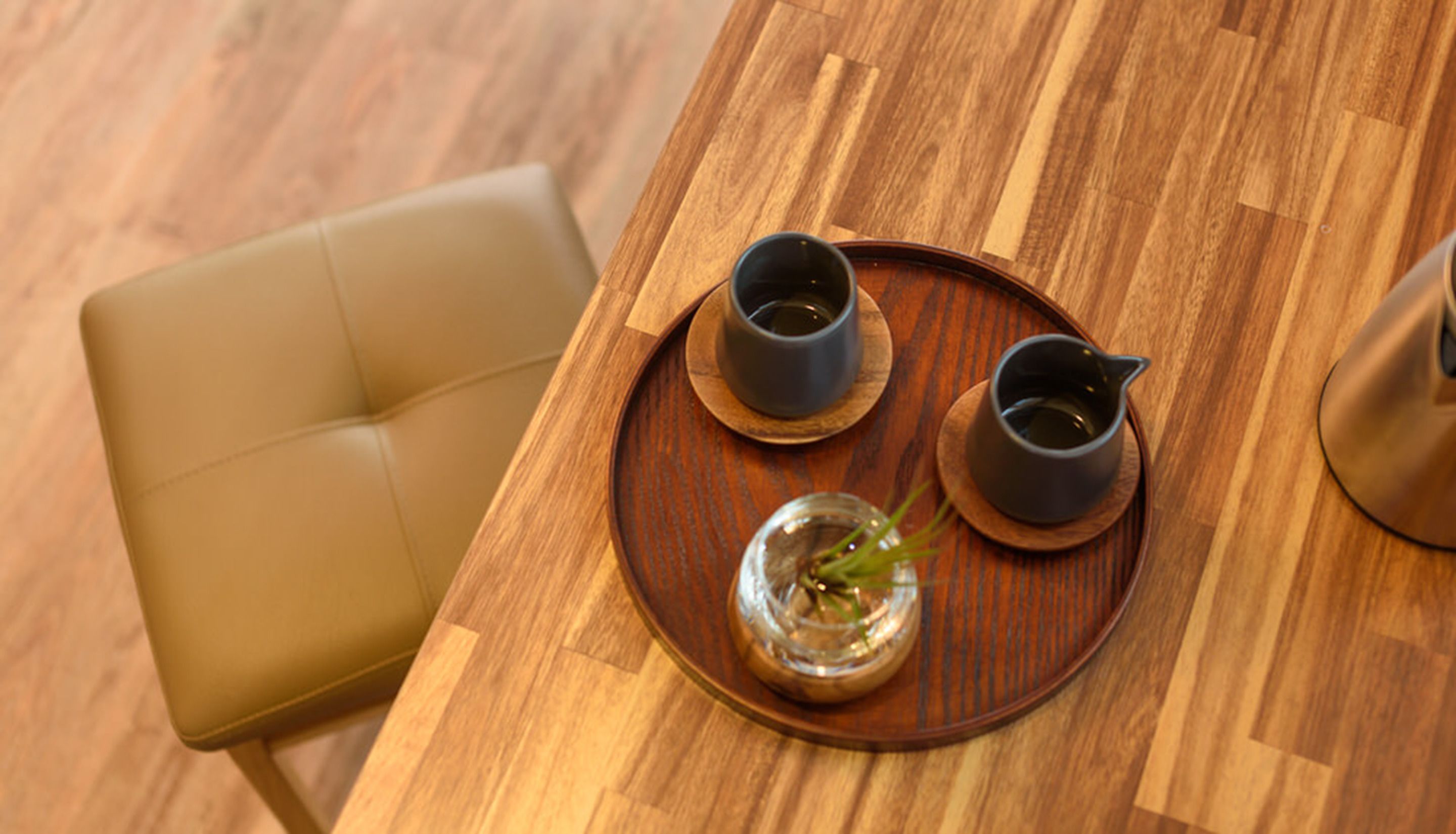 Uma mesa de jantar de madeira com duas xícaras pretas e um pequeno vaso com uma planta.