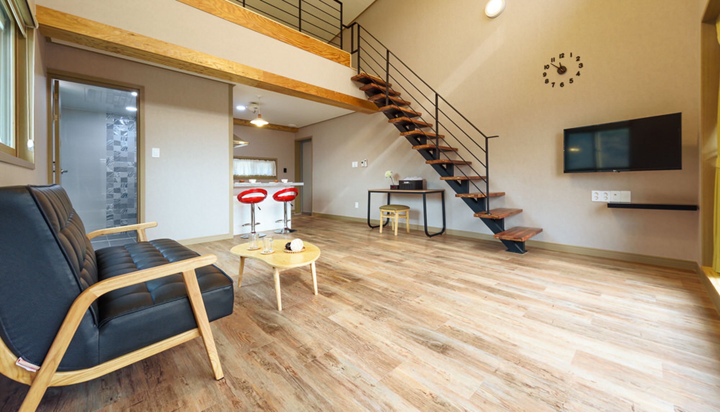 A spacious living area with a black leather sofa, a wooden coffee table, and a staircase leading to an upper level.