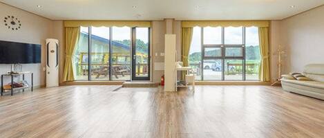 A spacious room with large windows, a flat-screen TV, and a sofa.