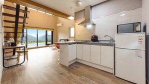 A modern kitchen with a large island, white cabinetry, a stainless steel range hood, and a view through the window. - Gyeongpoen Pension (Gangneung)