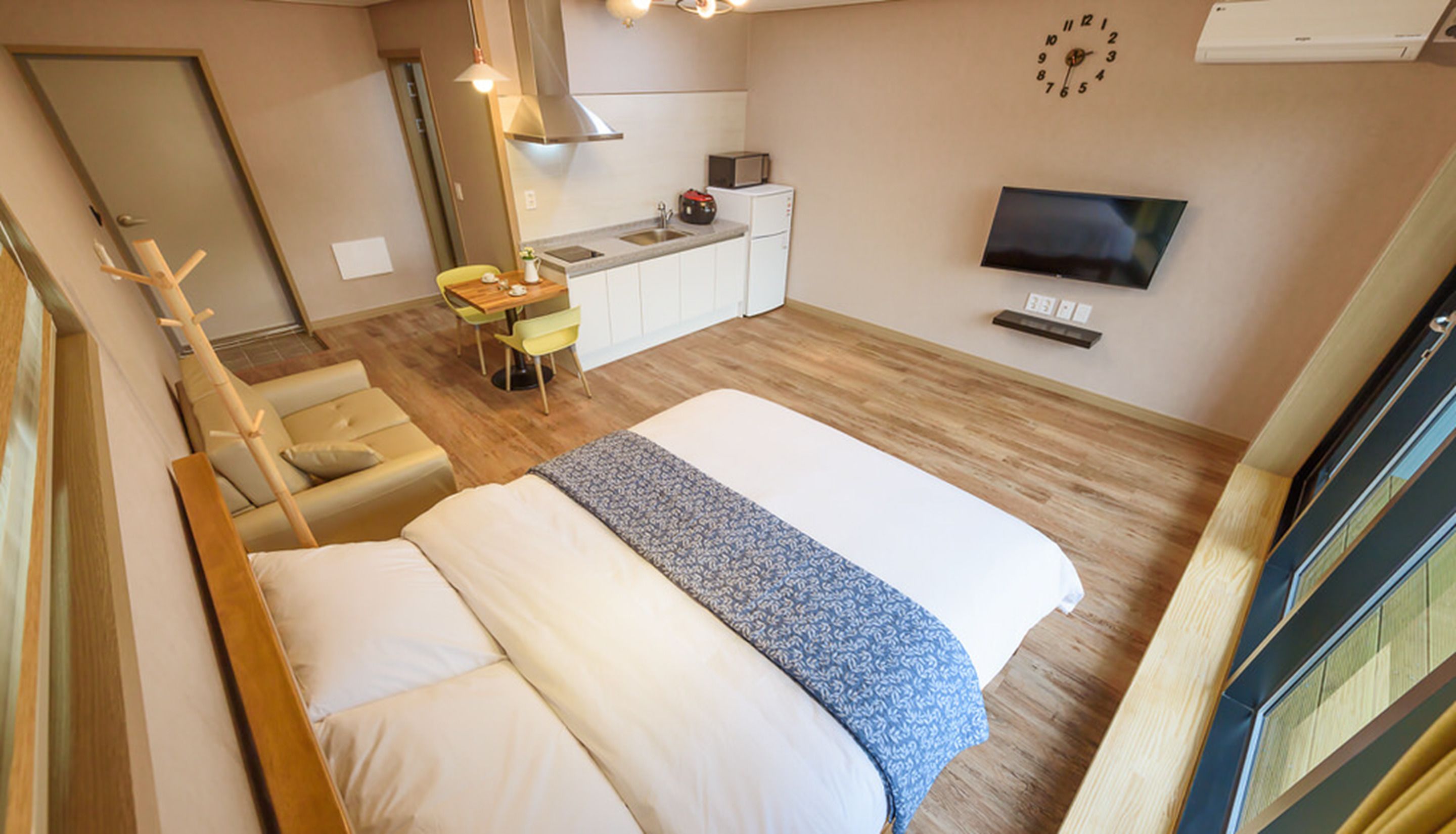 A compact hotel room with a bed, a small kitchenette, a TV, and a window.
