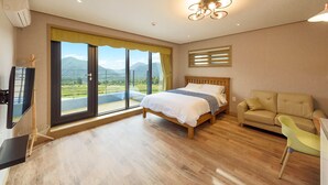 A bedroom with a bed, a sofa, a TV, and a balcony with a view of mountains. - Gyeongpoen Pension (Gangneung)