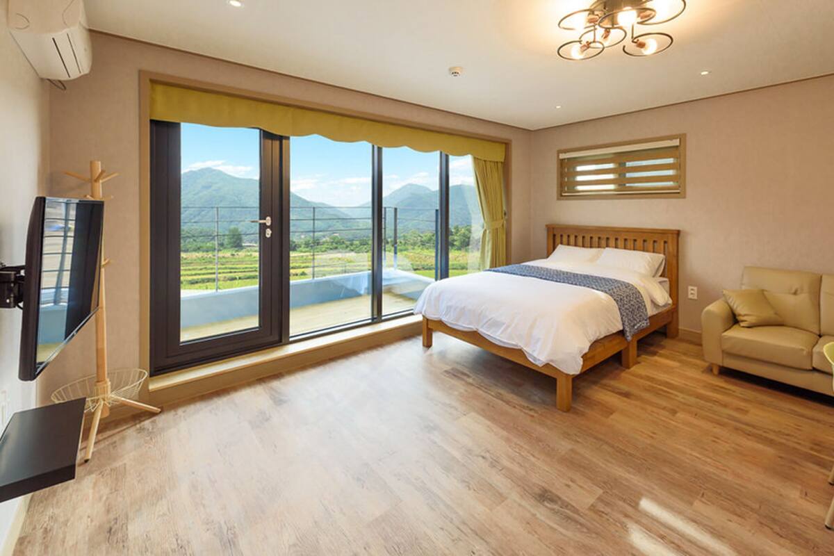 Ein Schlafzimmer mit Bett, Sofa, Fernseher und einem Balkon mit Bergblick.