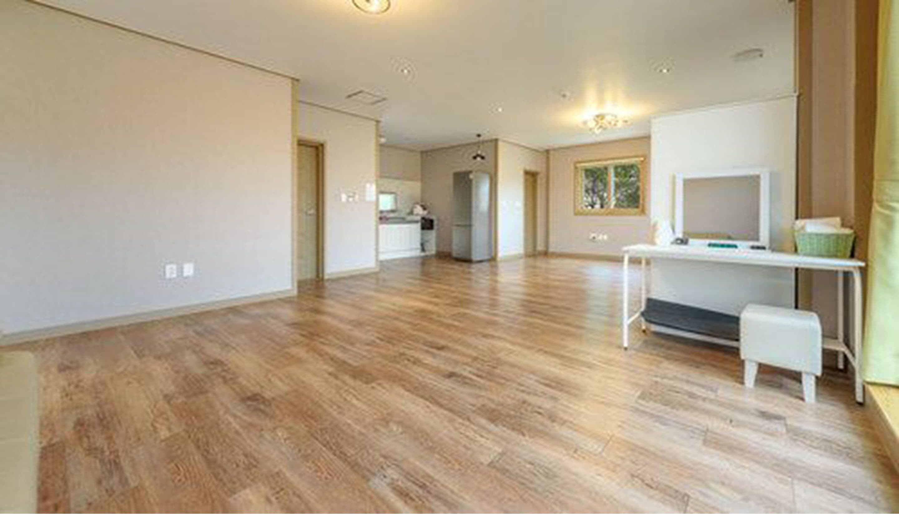 A spacious room with hardwood flooring, a kitchenette, and a large window providing natural light.